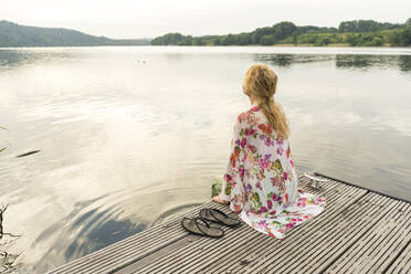 Junge Frau sitzt auf einem Steg an einem See - JOSF03623