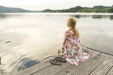 Young woman sitting on a jetty at a lake - JOSF03623