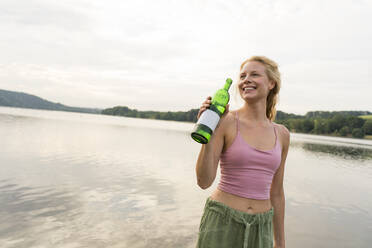 Glückliche junge Frau trinkt Wasser an einem See - JOSF03624