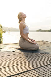 Junge Frau übt Yoga auf einem Steg an einem See - JOSF03631