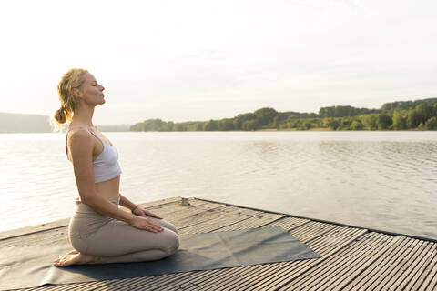 Junge Frau übt Yoga auf einem Steg an einem See, lizenzfreies Stockfoto