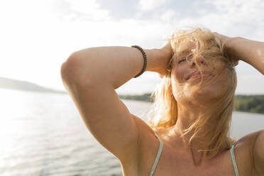 Young woman with windswept hair at a lake - JOSF03641