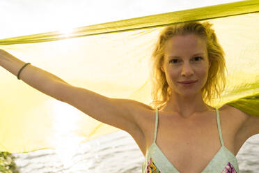 Portrait of young woman holding a cloth at a lake - JOSF03645