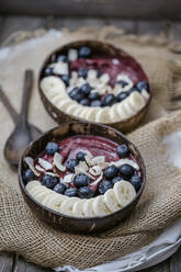 Hohe Winkelansicht von Eis mit Bananenscheiben und Blaubeeren in Schalen auf dem Tisch - STBF00377