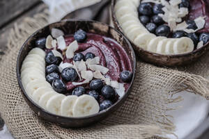 Nahaufnahme von Speiseeis mit Bananenscheiben und Blaubeeren in Schalen auf dem Tisch - STBF00378