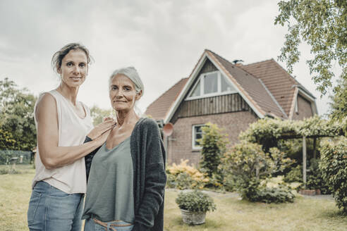 Mother and daughter standing in garden, inf ront of their house - JOSF03649