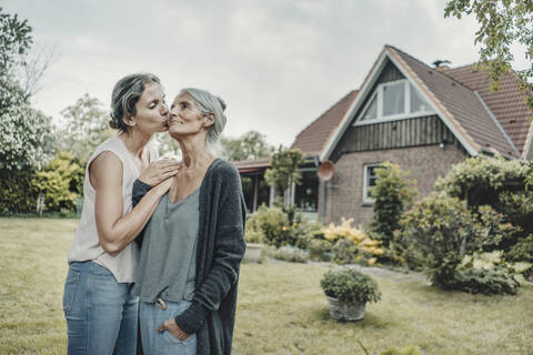 Tochter küsst Mutter im Garten, vor ihrem Haus, lizenzfreies Stockfoto