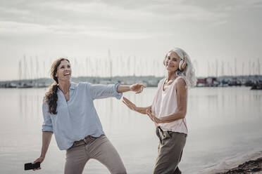 Mother and daughter spending a day at the sea, listening music - JOSF03665