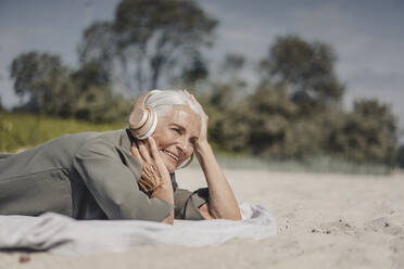 Senior woman listening music with headphones on the beach - JOSF03688