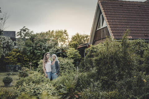 Mutter und Tochter stehen im Garten, vor ihrem Haus, lizenzfreies Stockfoto