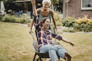 Mother pushing daughter, sitting in push cart, through the garden - JOSF03727