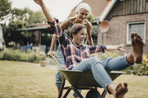 Mutter schiebt ihre Tochter, die in einem Kinderwagen sitzt, durch den Garten, lizenzfreies Stockfoto