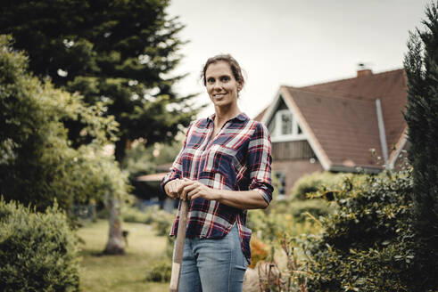 Stolze Hausbesitzerin steht mit einem Spaten in ihrem Garten - JOSF03730