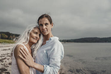 Mother and daughter spending a day at the sea, embracing on the beach - JOSF03743