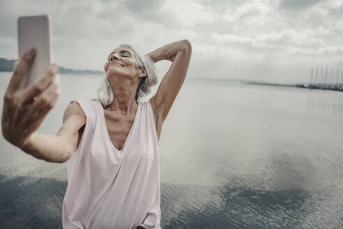 Senior woman taking smartphone selfies at the sea - JOSF03751