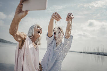 Mother and daughter havin fun on the beach, taking smartphone selfies - JOSF03757