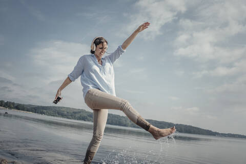 Frau mit Kopfhörern, die am Strand ins Wasser tritt, lizenzfreies Stockfoto
