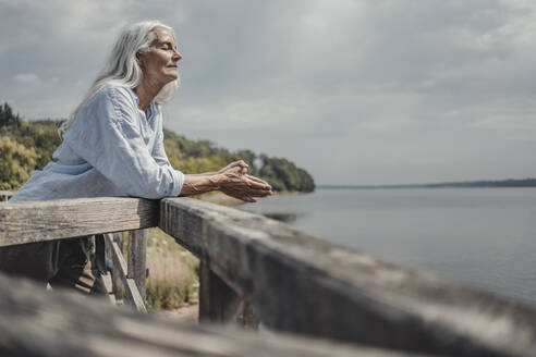 Senior woman standing on bridge, relaxing with eyes closed - JOSF03766