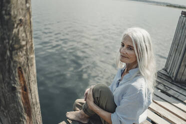Ältere Frau sitzt auf dem Steg und entspannt sich am Meer - JOSF03772