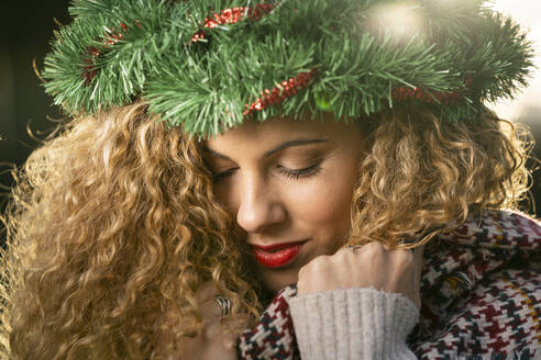 Porträt einer lächelnden jungen Frau mit Weihnachtskranz auf dem Kopf - DAMF00061