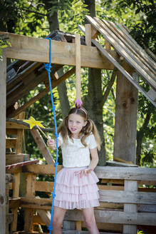 Girl dressed as a princess with crown and sceptre playing in a tree house - HMEF00552