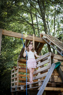 Girl dressed as a princess with crown and sceptre playing in a tree house - HMEF00555