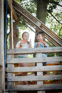 Mädchen und Junge essen Wassermelone im Baumhaus - HMEF00572