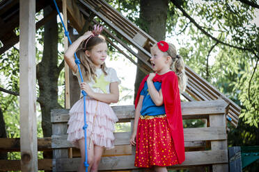 Girls dressed up as princess and superwoman playing in a tree house - HMEF00574