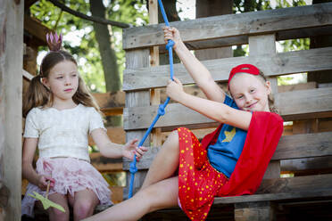 Als Prinzessin und Superfrau verkleidete Mädchen spielen in einem Baumhaus - HMEF00575