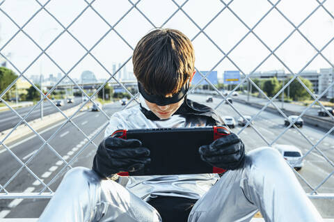 Boy disguised as superhero using games cosole above the streets of the city stock photo