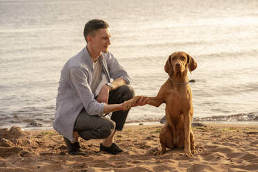 junger Mann mit seinem Hund am Strand, Hund gibt Pfötchen - VPIF01524