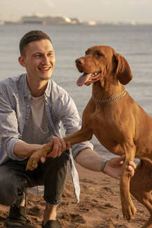 Young man with his dog at the beach, dog giving paw - VPIF01526