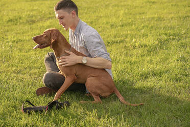 junger Mann mit seinem Hund, kuschelnd auf einer Wiese - VPIF01530