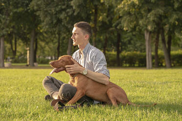 junger Mann mit seinem Hund, kuschelnd auf einer Wiese - VPIF01531