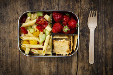 Directly above shot of pasta with strawberries and crackers in lunch box on wooden table - LVF08259