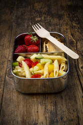 High angle view of pasta with strawberries and crackers in lunch box on wooden table - LVF08260