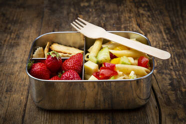 Nahaufnahme von Nudeln mit Erdbeeren und Crackern in einer Lunchbox auf einem Holztisch - LVF08261