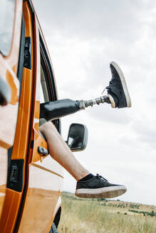 Die Beine eines jungen Mannes mit Prothese baumeln aus dem Fenster eines Wohnmobils - CJMF00012