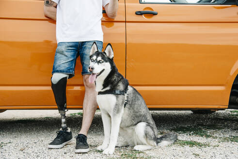 Young man with dog wearing leg prosthesis at camper van - CJMF00016