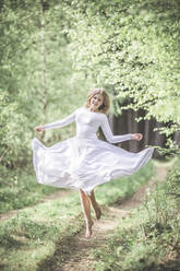Young woman wearing white dress, dancing in the forest - STBF00389