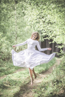 Junge Frau in weißem Kleid, tanzend im Wald - STBF00389