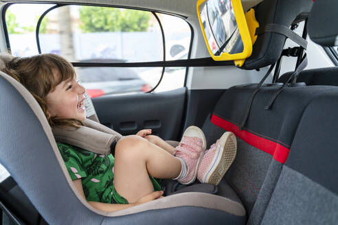 Lachendes Kleinkind, das in einem Autositz sitzt und in einen Spiegel schaut - GEMF03148