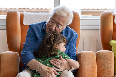 Grandmother hugging her granddaughter in living room - GEMF03153