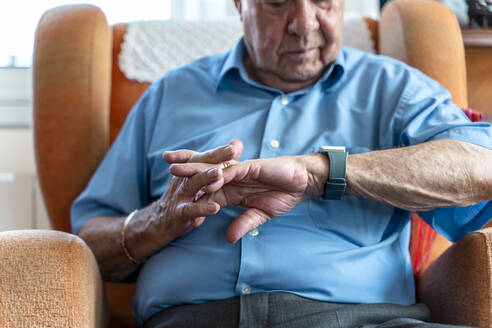 Älterer Mann, der zu Hause ein intelligentes Notfallalarmarmband um das Handgelenk trägt - GEMF03159