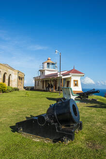 Blick auf eine Kanone an Land mit Fort King George im Hintergrund vor blauem Himmel, in Scarborough, Trinidad und Tobago, Karibik - RUNF03188