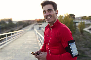 Jogger with smartphone in arm pocket, holding smartphone and looking at camera - JSRF00598