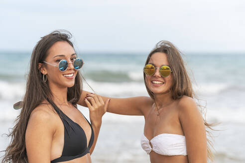 Zwei glückliche Freundinnen mit Sonnenbrillen am Strand - DLTSF00133