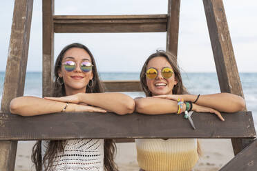Porträt von zwei glücklichen Freundinnen an einer Holzleiter am Strand - DLTSF00141