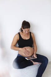 Junge schwangere Frau mit Ultraschallbild ihres ungeborenen Babys auf ihrem Tablet - HMEF00579