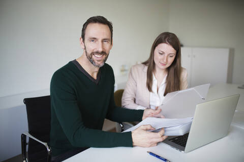 Porträt eines lächelnden Geschäftsmannes und eines Angestellten, der am Schreibtisch im Büro arbeitet, lizenzfreies Stockfoto